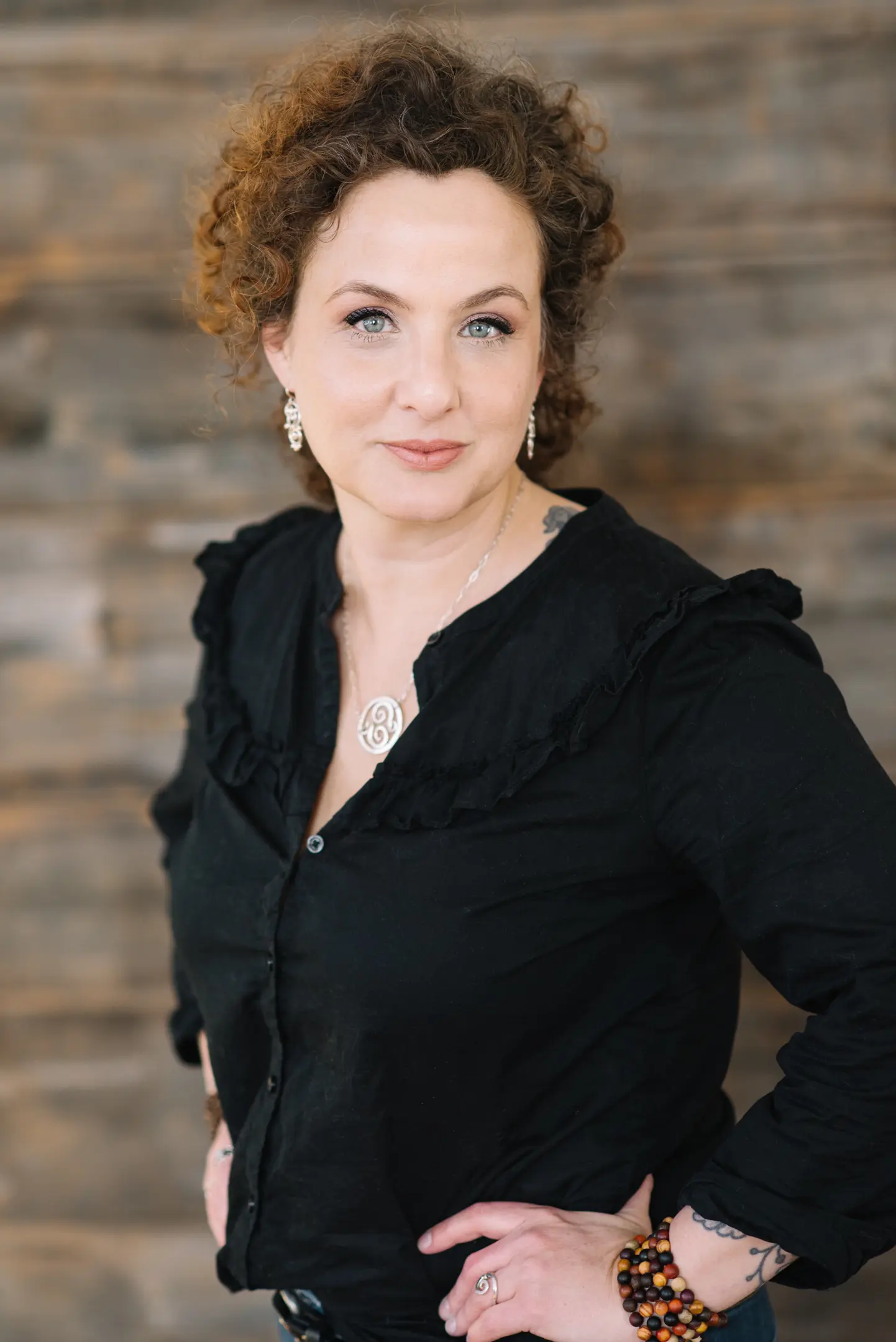 Erin elizabeth | crownsville media - seo, ai visibility & digital marketing for small business owners | crownsville media - seo, ai visibility & digital marketing for small business owners Portrait of a woman with curly red hair in a black blouse silver jewelry standing with hands on hips against a wood paneled backdrop
