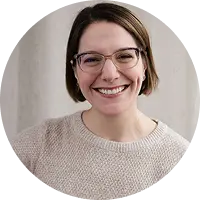 Smiling woman with short brown hair and glasses wearing a beige knit sweater facing the camera