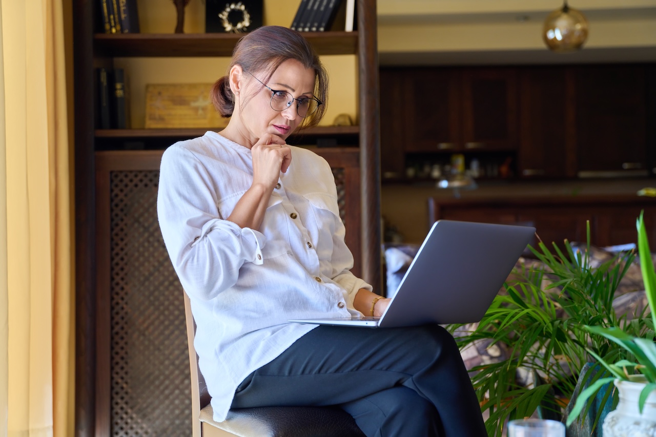 Serious middle aged business woman working with laptop sitting in home office