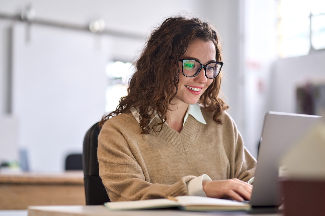 Young happy woman therapist sitting at desk using laptop